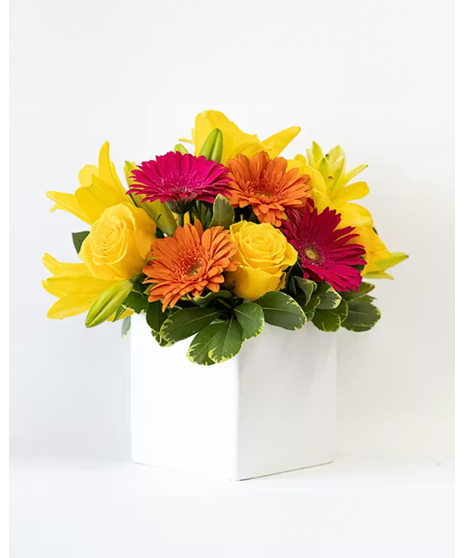Bright bouquet of gerbera daisies, roses and  lilies in a clear glass cube vase