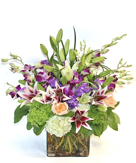 Purple dendrobium orchids, peach roses, green hydrangea and more in a leaf-lined vase