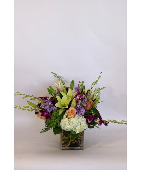 Purple dendrobium orchids, peach roses, green hydrangea and more in a leaf-lined vase