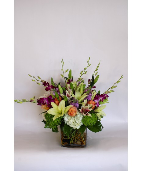Purple dendrobium orchids, peach roses, green hydrangea and more in a leaf-lined vase