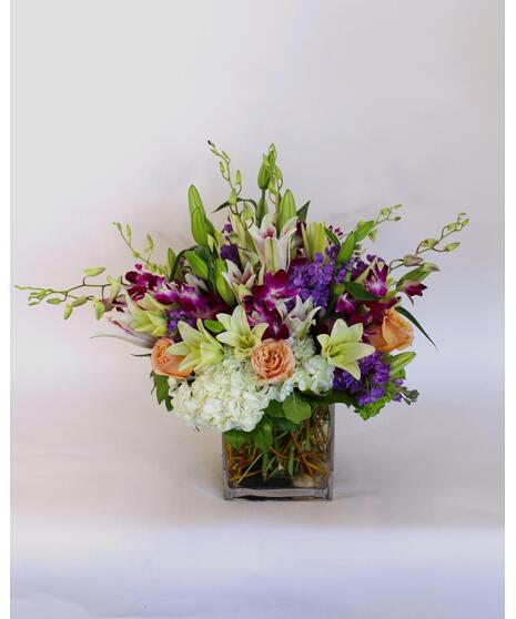Purple dendrobium orchids, peach roses, green hydrangea and more in a leaf-lined vase