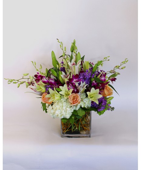 Purple dendrobium orchids, peach roses, green hydrangea and more in a leaf-lined vase